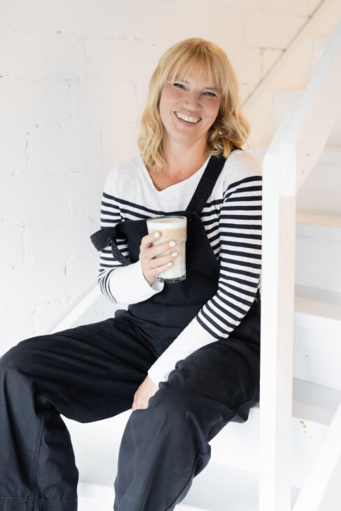 Jutta Mesch lächelnd, auf einer Treppe sitzend mit einer Latte Macchiato in der Hand.