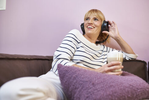 Blonde Frau mit Kopfhörer sitzend auf einem Sofa in Pink- und Lilatönen