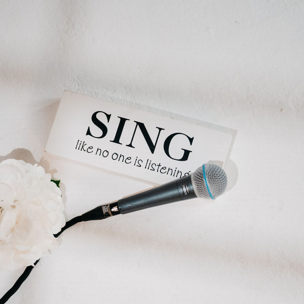 Mikrofon mit einem weißen Schild mit der Aufschrift "Sing like no one listening" mit weißer Blume dekorativ auf den Boden gelegt