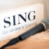 Schild mit der Aufschrift "Sing like no one is listening" mit einem liegenden Mikrofon davor in Szene gesetzt