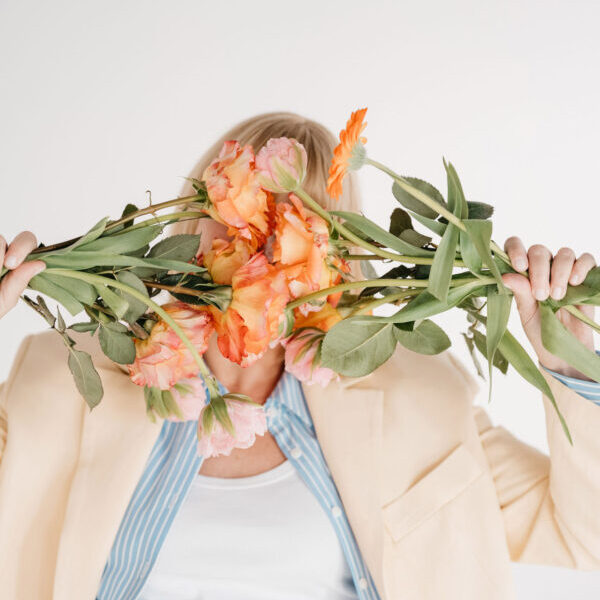 Frau im gelben Hosenanzug mit leuchtenden Blumen vor dem Gesicht.