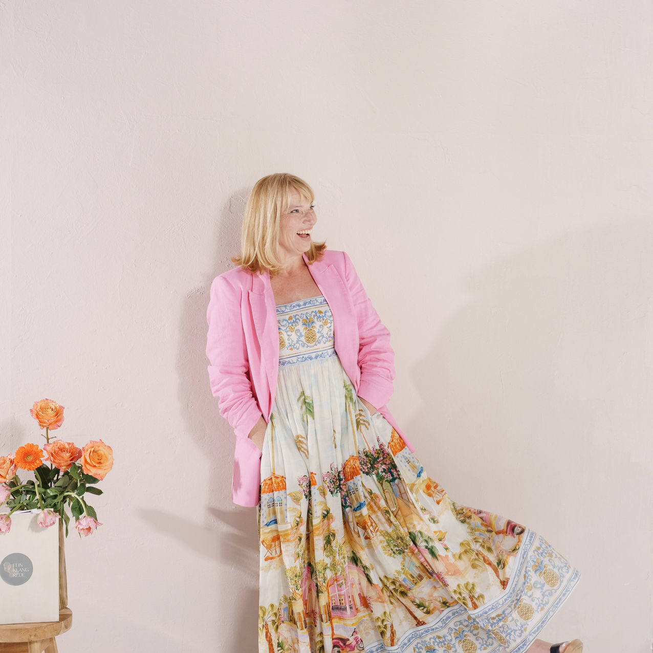 Lachende Frau in buntem Sommerkleid mit rosafarbenem Blazer.